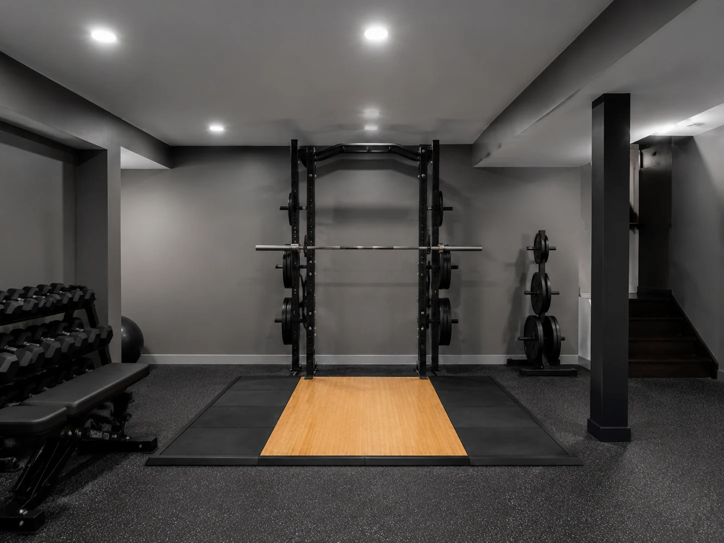 Basement gym layout with squat rack, platform flooring, and bright LED lighting