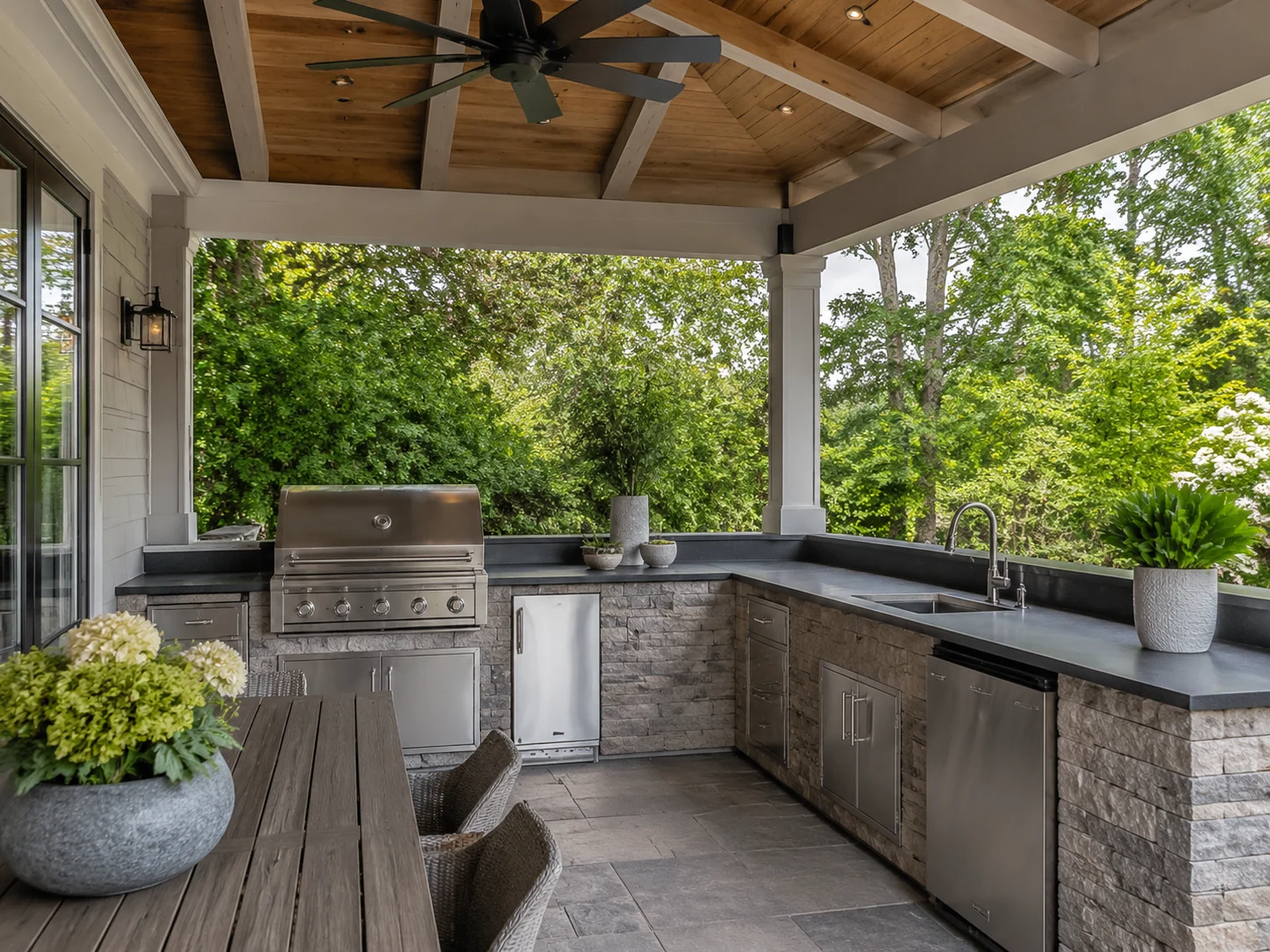 Covered outdoor kitchen under a roof with a grill, sink, and fan